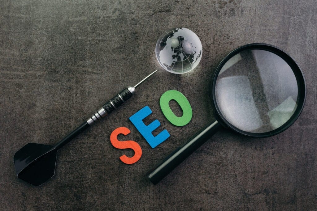 SEO Conceito de otimização de mecanismo de busca, dardo apontando para um globo, lupa e palavra do alfabeto SEO em vermelho, azul e verde sobre fundo de quadro-negro de cimento escuro